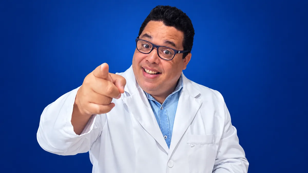 Professor Thiago Santos de jaleco apontando para a frente, em fundo azul